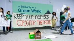 Protestors standing in front of a COP30 sign, holding a banner that reads 'Keep your promises. COP30 for the people'.