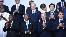 A group of men of different nationalities, all in formal dress, clap and smile as they pose for a photo.