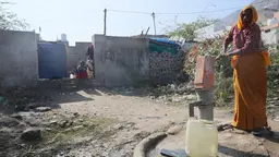 Woman pumping water into a plastic canister. She is wearing a traditional saree.