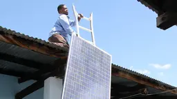 A man on top of a rook hauls up a solar panel.