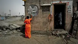 Woman worker in a stone quarry wearing a bright orange saree is making a phone call using a land line outside a building.