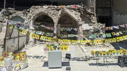 Bright, small packets hang down from ropes in front of a partly destroyed building.