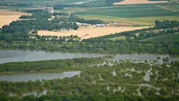 An aerial view of a river that has flooded the surrounding area, showing fields and houses partly submerged by water.