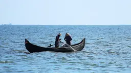 Two people on a fishing boat in India, catching fish with a net.