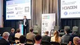 A man stands at a podium, in front of 2025 London Climate Resilience Finance Summit branding, and address a seated audience.