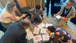 Group of people sitting on the floor, discussing ideas and writing things down on A4 papers.