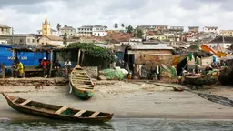 Fishing community in Ghana. People standing around informal huts on the sea front, with boats dragged on the shore.