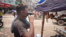 A rickshaw puller in Dhaka pauses by the roadside to drink water before continuing his route.