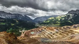 A long-range photo of a landscape showing tiered levels that denote mining in front of mountains.   