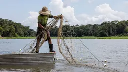 A man on a small boat maintains his balance as he draws in a net.