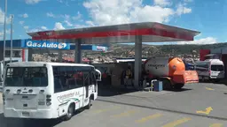 A bus queues outside a petrol station at which a tanker is filling up with petrol 
