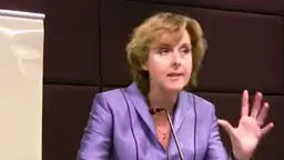 A woman gives a speech, raising her hand to make a dramatic point.
