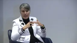 A seated woman puts her hands together in thought as she answers a question from an audience.
