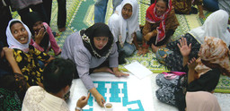 Women are gathered around a paper with squares on it talking.