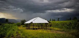 A church under construction sits on a verdant green field with dark grey storm clouds behind. 