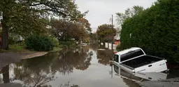 A pick up truck lies mostly submerged under a water in a flooded street. 