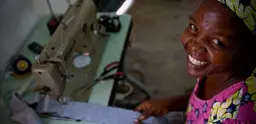 A smiling woman from Kenya sits beside her sewing machine. 