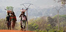 Women walk along a red dirt road in Benin.  