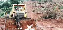 A man in Uganda stands by a digger sitting next to a dirt road. 