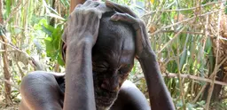 A Batwa man sits with his hands cupping his head