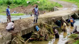Men stand on a river bank and in the water to clear detritus 