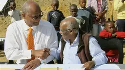 Jockin Arputham, right, signs documents with Stellenbosch Mayor Sidego in South Africa