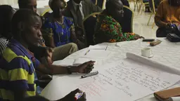 Delegates at CBA12 in Malawi gather around a table and write on a document