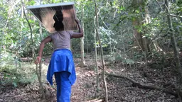 A woman in Malawi carries a solar panel above her head through a forest path
