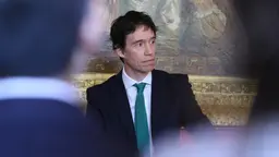 A photo of a man addressing a conference, pictured through the heads of those listening