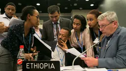 A huddle of people gather around one person to give advice and discuss negotiating tactics