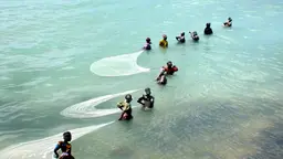 Women pulling fishing nets through shallow water