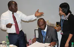 Three people gather to discuss a document one of them is holding in his hand