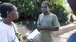 Conversation between a woman with a notebook and a man, with trees in the background