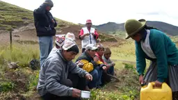 Peruvian men and women on a mountainside, pouring water on the earth