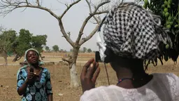 Two women in an African landscape: one with a camera filming another with a microphone