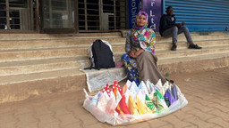 A woman sitting on steps, with colourful handkerchiefs arranged in front of her