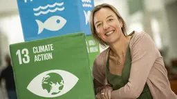 Tara Shine is photographed smiling next to boxes on which is written 'climate action'