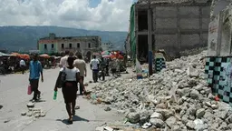People walk past ruined buildings