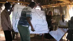 Men present findings on a large map at the front of a community meeting