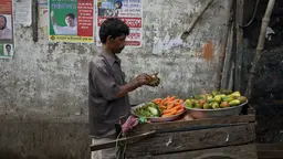 A vegetable seller with a food truck peels a cucumber