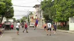 A group of young men play volleyball in the middle of the street, with a makeshift net