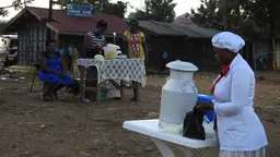 Women are sat at tables selling food a distance apart
