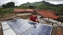 Indian woman does maintenance work on solar panel, with mountains in the background.
