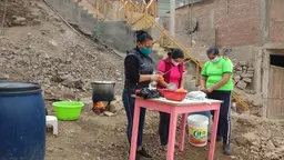 Three women standing on a patch of open land, peeling vegetables.