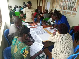Men and women sitting around a table, writing on poster-like papers