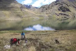 A family harvesting potatoes in front of a lake, with a landscape of mountains in the background.