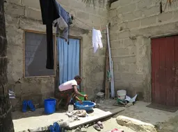 Woman washing dishes in a bowl outside.