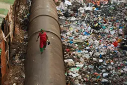 Woman walking on a pipe with garbage around.
