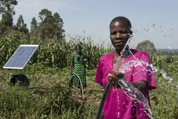 Woman looking to the front holding a water hose, a solar panel in the background