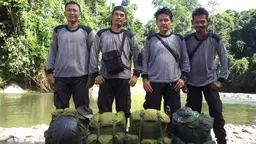 Four men pose with their backpacks on the floor
